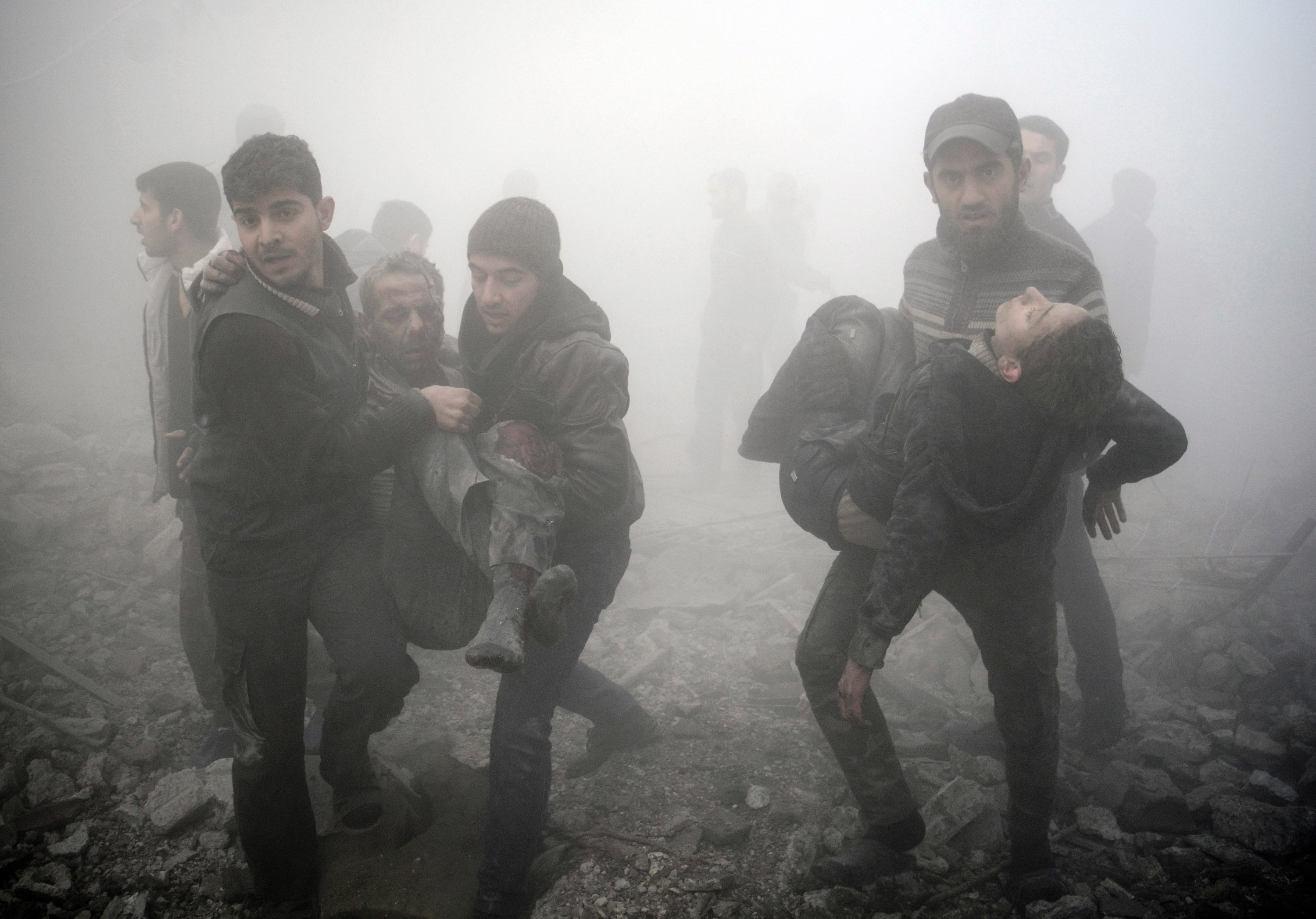 Syrian men carry injured victims following a reported air strike on the besieged rebel-held town of Douma, northeast of the capital Damascus on January 21, 2015. Rebel-held towns such as Douma face frequent aerial and tank bombardment and the siege means food is scarce and medical facilities are ill-equipped to handle either illness or injury. AFP PHOTO / SAMEER AL-DOUMY / AFP PHOTO / - AND SAMEER AL-DOUMY